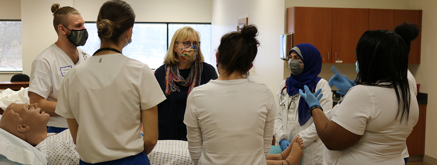 Six students, all wearing facemasks, listen to Lori Glenn inside of a classroom at the Novi Campus.