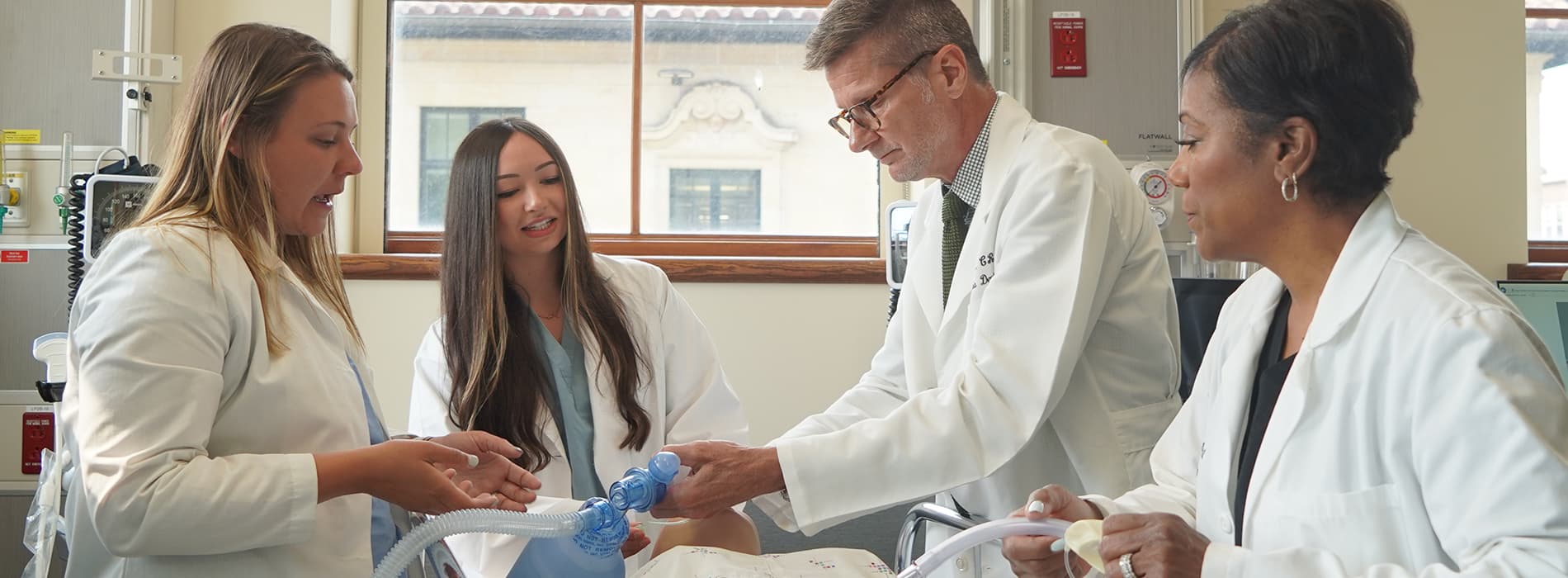 students and prof in a sim lab working on a manikin